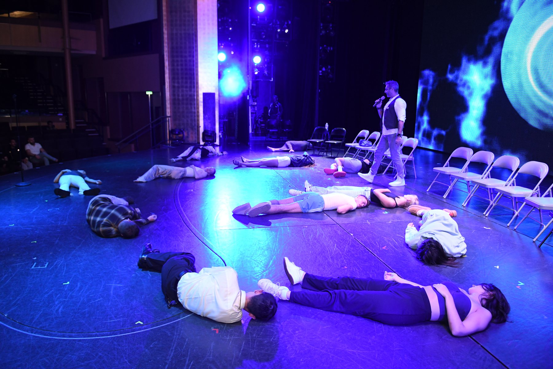 Hypnotised volunteers lying across a cruise theatre stage under blue light