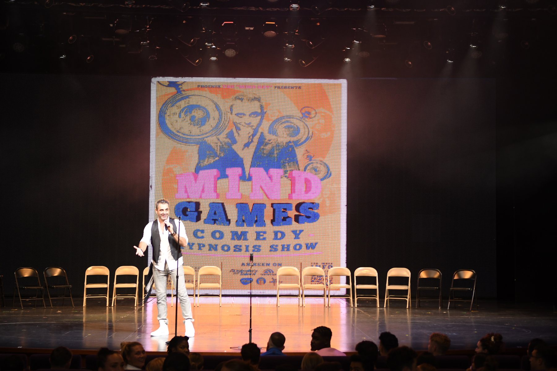 Volunteers slumped asleep across a row of chairs in front of the Mind Games Comedy Hypnosis Show screen