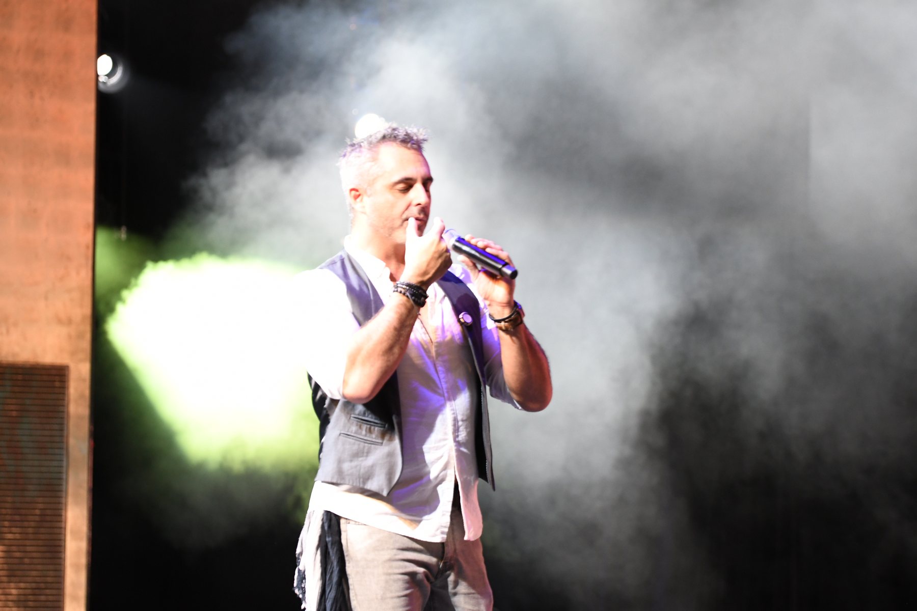 Phoenix on a smoke-filled stage with a microphone, lit from behind